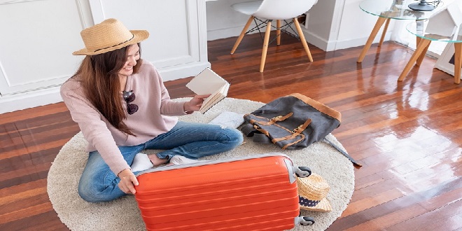 Young asian woman traveler prepare things into orange suitcase for holiday vacation at home.backpacker travel concept